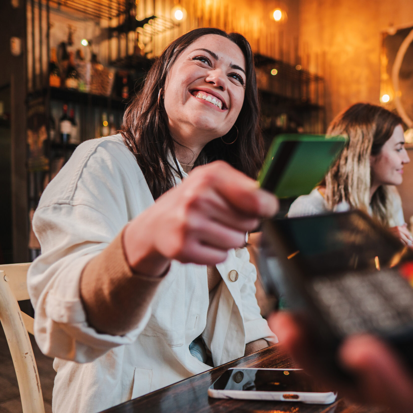 Happy young woman paying bill with a contactless credit card in a restaurant. Female smiling holding a creditcard and giving a payment transaction to the cashier.